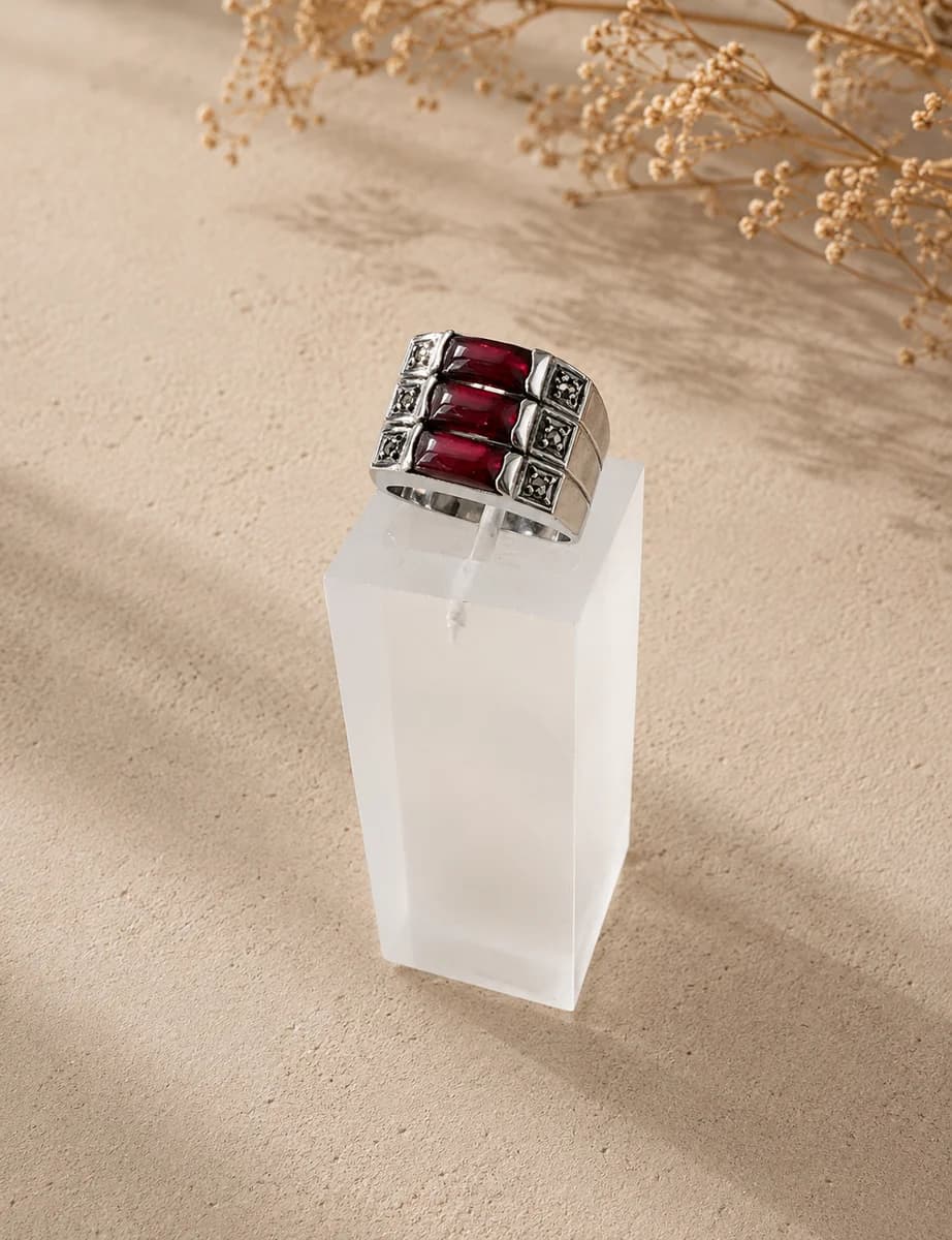 Anel de prata 950 com banho de ródio, granadas vermelhas lapidadas em rectangular e marcassita em design Art Déco, exposto em suporte de acrílico branco